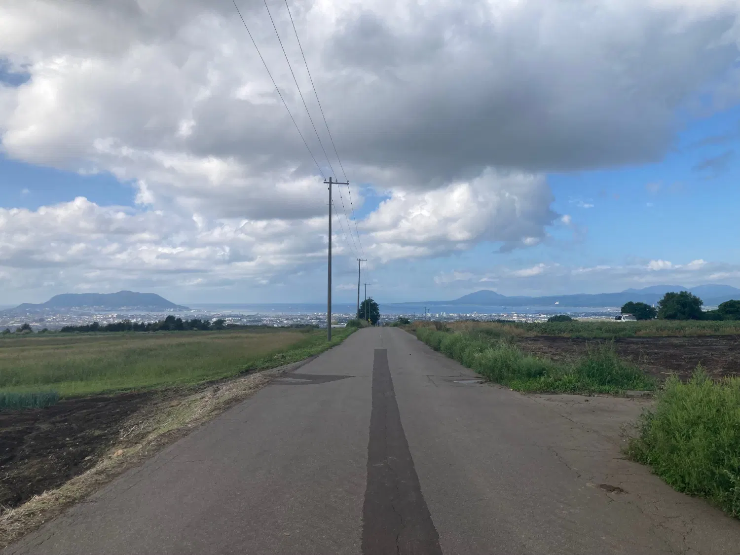 丘の上に真っ直ぐに伸びる道と、函館山と海が見える