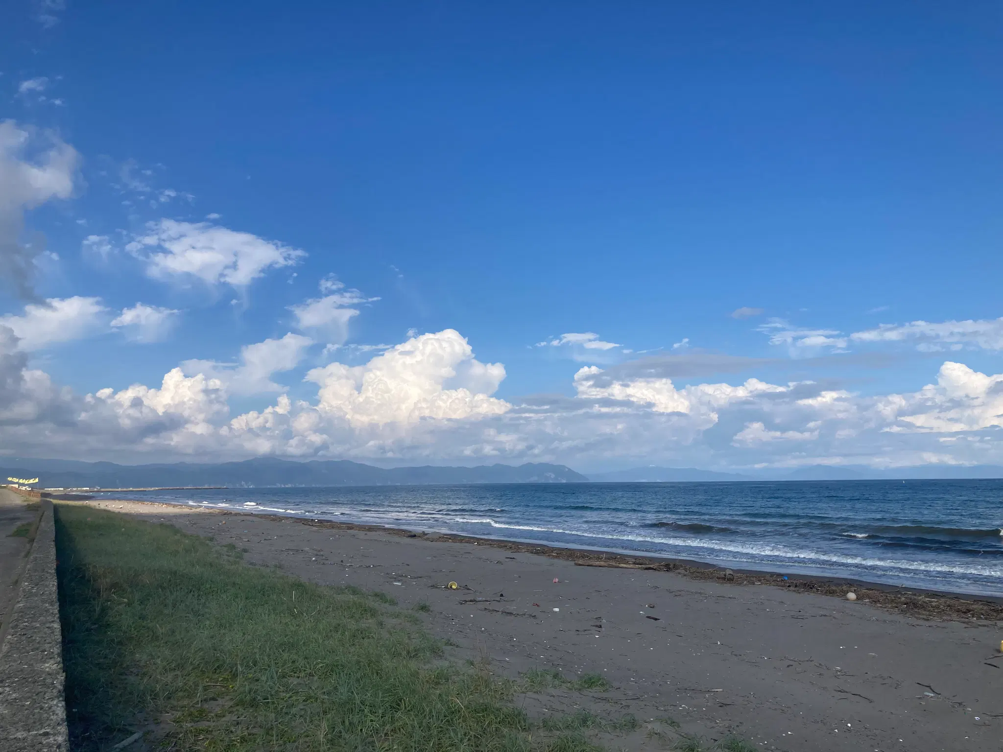 防潮堤の上から眺める砂浜と海、奥に山が見える