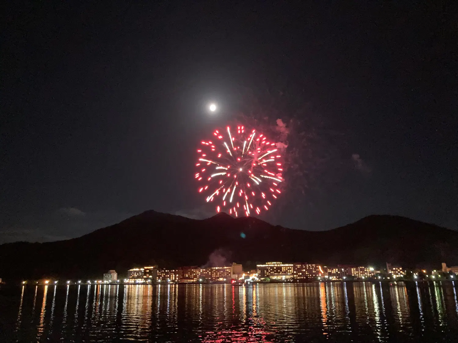 明るい赤色の花火、奥に有珠山と満月が見える